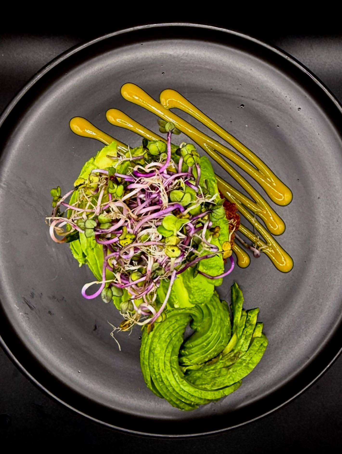Avocado fan with sprouts and mustard sauce dots.