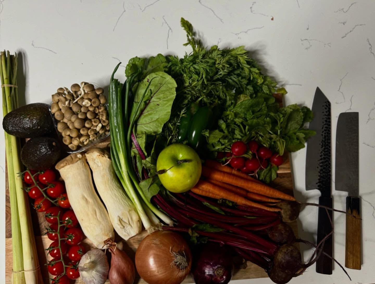 Mise en place: lemongrass, mushrooms, fresh produce, knives arranged on a marble counter.